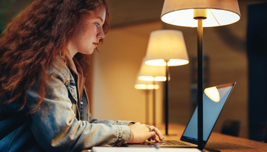 young lady using a laptop in a library at night | open+