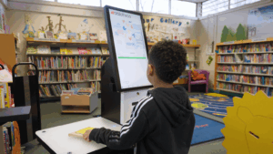 A child uses a Bibliotheca selfCheck 3000 kiosk in a public library, showing how modern self-service technology supports accessibility and independence.